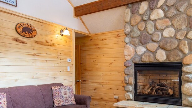 A cabin interior with a stone fireplace, wooden walls, a sofa with patterned cushions, and a welcome sign. - Located on the river, facing the Mountains (Red River)
