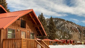 A wooden cabin with a red roof, a wooden deck, and a staircase leading to the entrance. - Located on the river, facing the Mountains (Red River)
