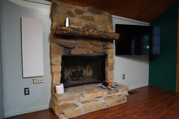 A stone fireplace with a TV mounted above it, a whiteboard on the wall, and a wooden floor. - Peaceful Smoky Mountain Cabin Near Cades Cove (Townsend)