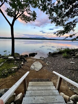 Un escalier en bois mène à une plateforme au bord du lac, d’où l’on peut admirer un lac paisible et des montagnes lointaines.