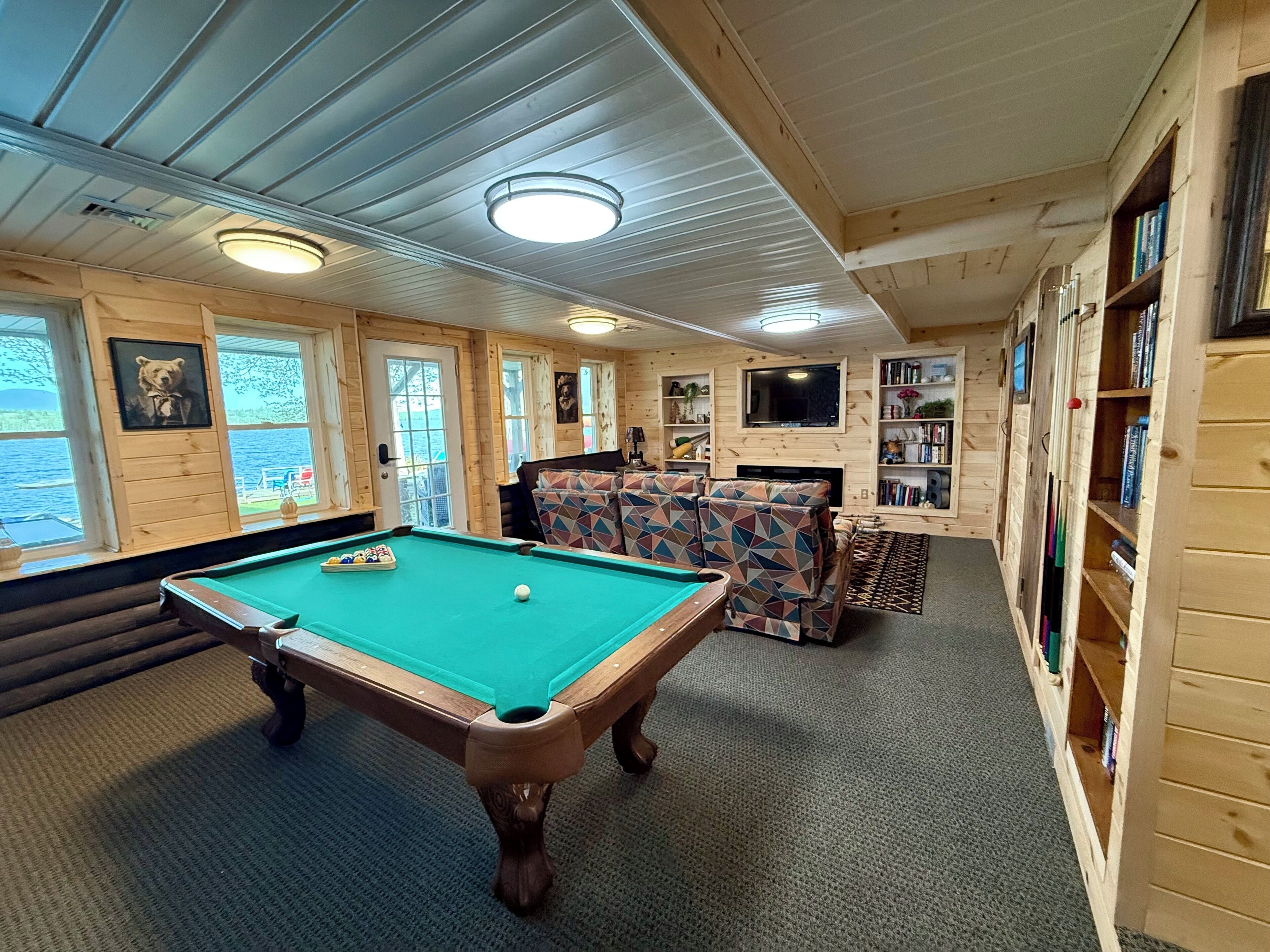A wooden interior with a pool table, a sofa, and bookshelves.