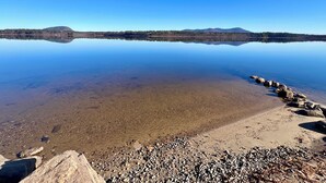 A calm lake with clear reflections, a rocky shoreline, and distant mountains.