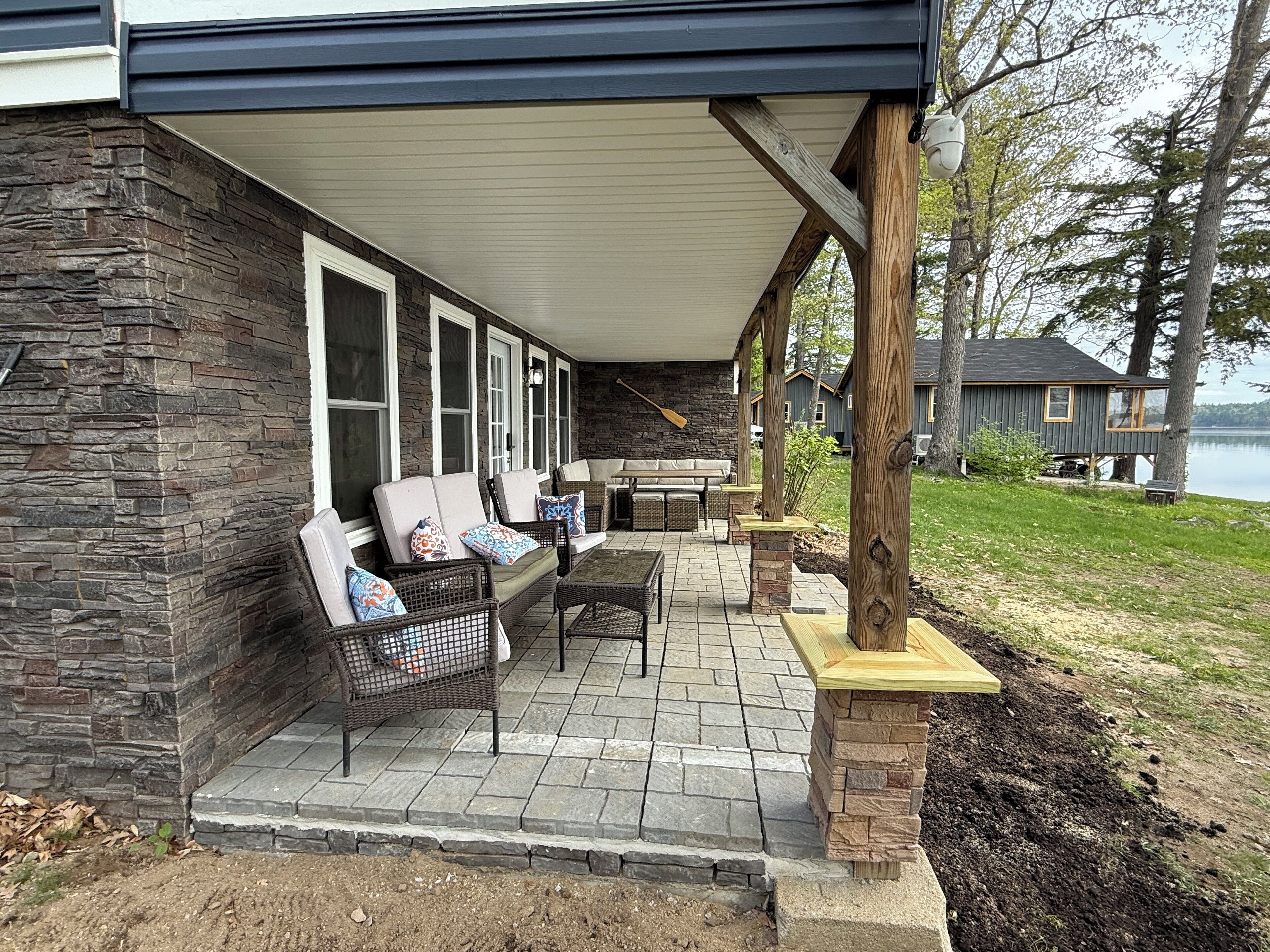 A covered patio with outdoor furniture, stone walls, and a view of a lake.