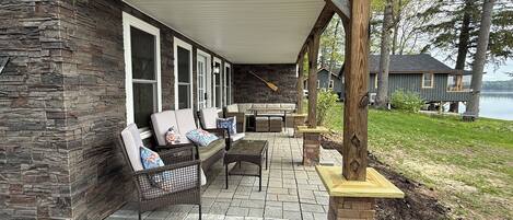 A covered patio with outdoor furniture, stone walls, and a view of a lake.