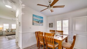 A dining area with a wooden table and chairs, a ceiling fan, and a beach-themed painting on the wall. - Sunny Fort Myers Home w/ Screened-In Porch & Grill (Fort Myers)