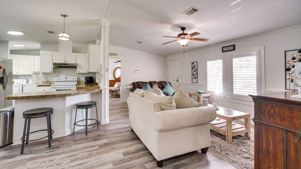 A spacious living area with a large sofa, a wooden coffee table, and a kitchen area with white cabinets and a granite countertop. - Sunny Fort Myers Home w/ Screened-In Porch & Grill (Fort Myers)