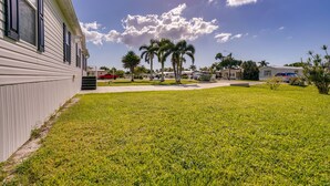 A grassy area with palm trees, a building with large windows, and a clear sky. - Sunny Fort Myers Home w/ Screened-In Porch & Grill (Fort Myers)