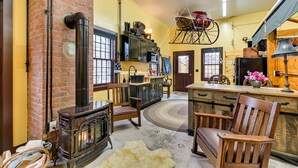 A rustic interior with a brick wall, wooden furniture, a fireplace, and a hanging chair. - Unique Finger Lakes Converted Horse Barn w/ Patio! (Geneva)