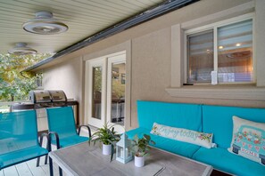 Une terrasse extérieure avec une table, des chaises, un barbecue et un canapé bleu agrémenté de coussins.