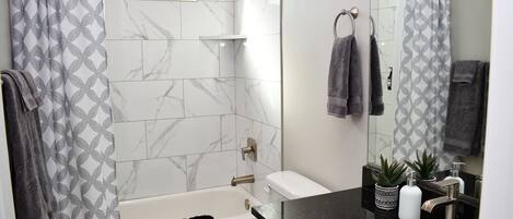 A modern bathroom with a bathtub, toilet, and sink. There are towels and a shower curtain.