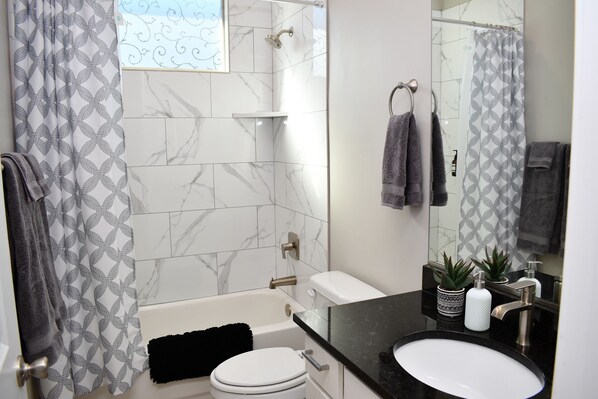 A modern bathroom with a bathtub, toilet, and sink. There are towels and a shower curtain. - 4BR Oasis • Heated Pool and Spa • Near Golf & Casinos (Mesquite)