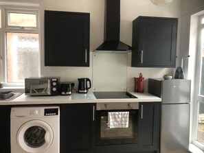 Compact kitchen with a washing machine, microwave, coffee maker, and small oven, offering convenient storage and appliances.