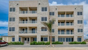 A multi-story residential building with balconies, a palm tree in the foreground, and a parked car. - Gloednieuw Appartement met Zeezicht. Fantastisch Gelegen 5 min van the Beach (Oranjestad)