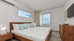 A modern bedroom with a wooden bed, a nightstand, a dresser, and a TV on the wall. - Gloednieuw Appartement met Zeezicht. Fantastisch Gelegen 5 min van the Beach (Oranjestad)