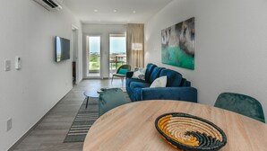 A modern living room with a blue sofa, a round wooden table, and a large abstract painting. - Gloednieuw Appartement met Zeezicht. Fantastisch Gelegen 5 min van the Beach (Oranjestad)