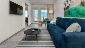 A modern living room with a blue sofa, a flat-screen TV, a round coffee table, and a large abstract painting. - Gloednieuw Appartement met Zeezicht. Fantastisch Gelegen 5 min van the Beach (Oranjestad)