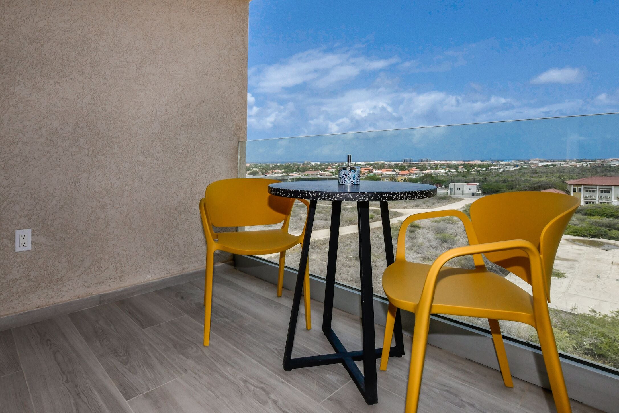 A balcony with a round table and two yellow chairs, overlooking a distant landscape.