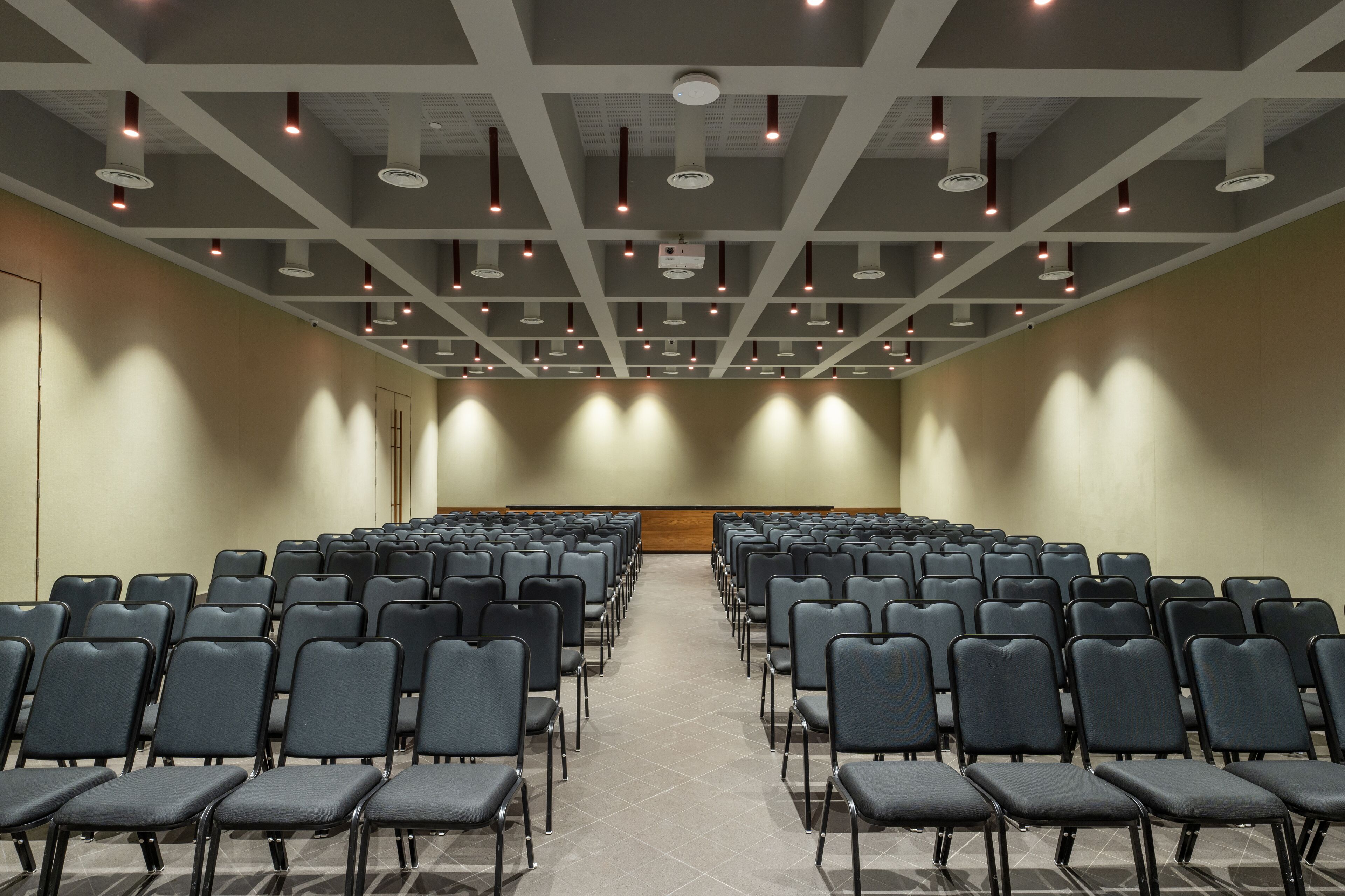Un salón de conferencias con filas de sillas, un atril y luces en el techo.