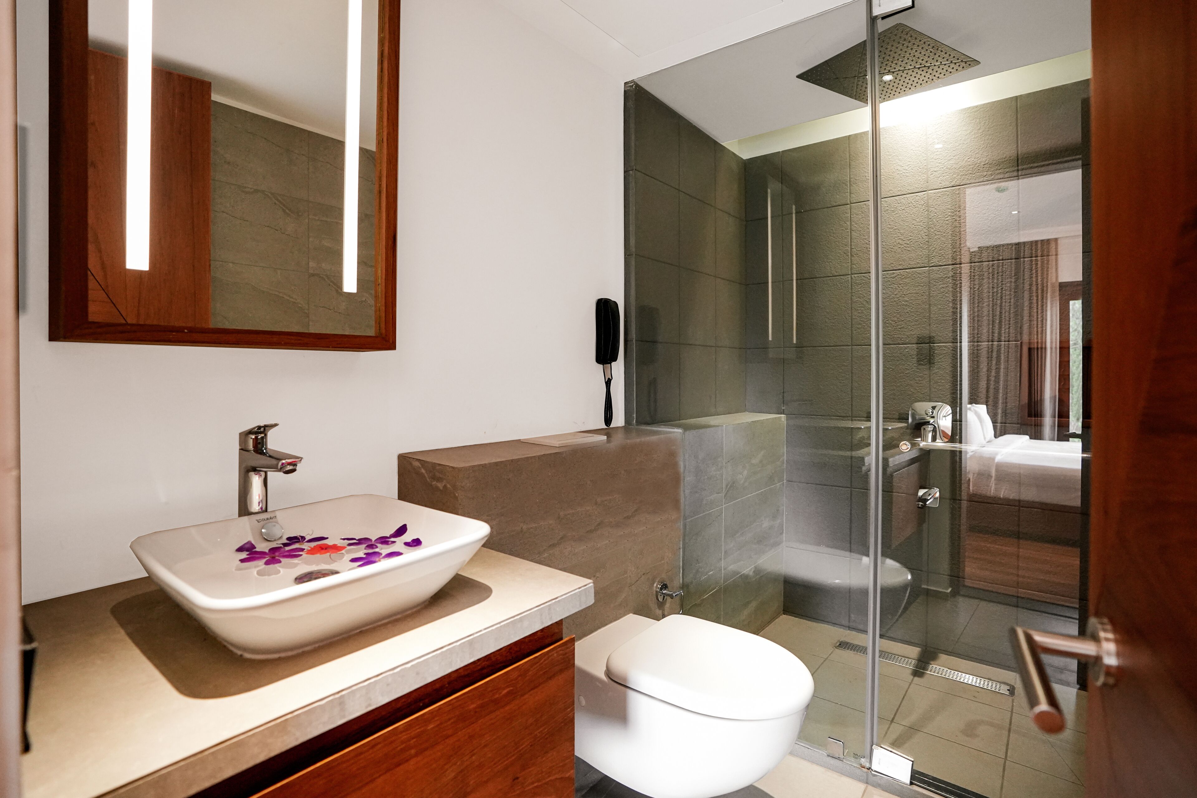 Un bagno moderno con box doccia in vetro, lavandino bianco con decorazioni floreali e mobile vanitario in legno.