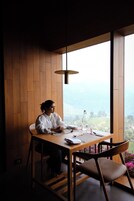 Una persona sentada a una mesa de madera con vistas a un paisaje montañoso a través de grandes ventanales.