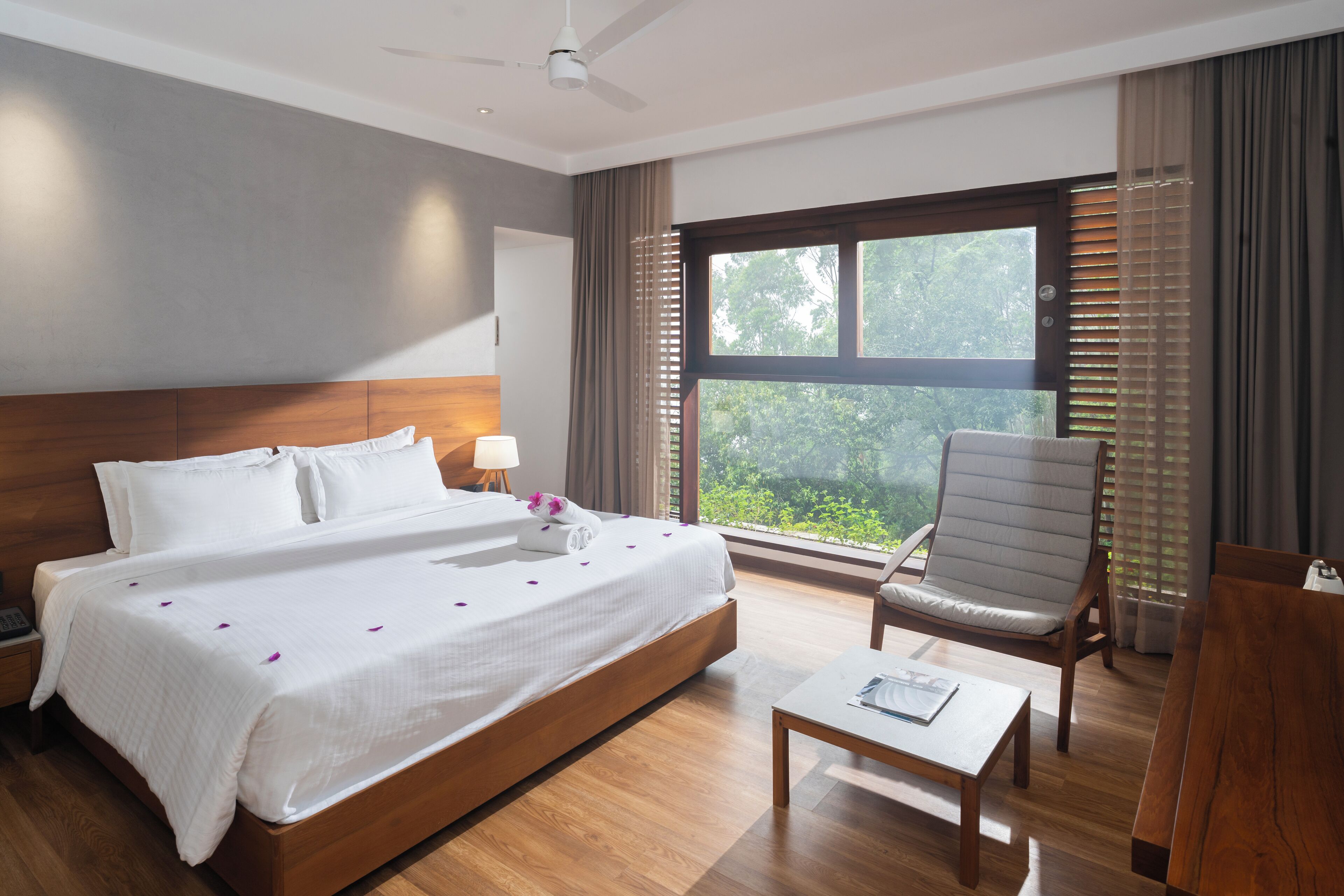 Ein Hotelzimmer mit einem großen Bett, einem Sessel, einem Couchtisch und einem Fenster mit Blick auf Grünflächen.