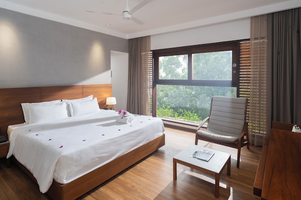 Ein Hotelzimmer mit einem großen Bett, einem Sessel, einem Couchtisch und einem Fenster mit Blick auf Grünflächen.