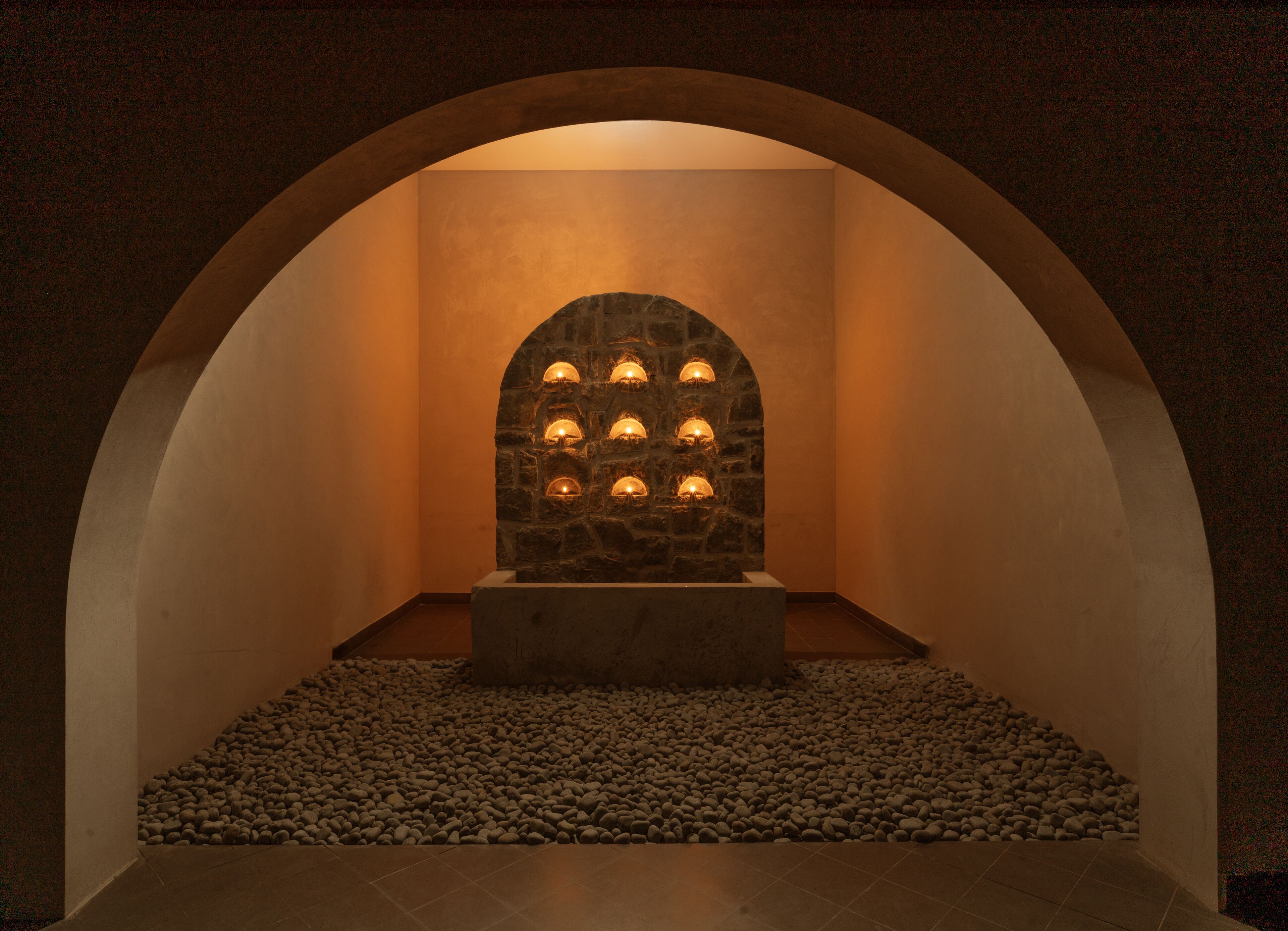 A stone wall with multiple lights, an arched ceiling, and a pebble floor.