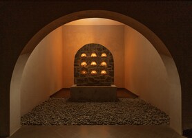 A stone wall with multiple lights, an arched ceiling, and a pebble floor.