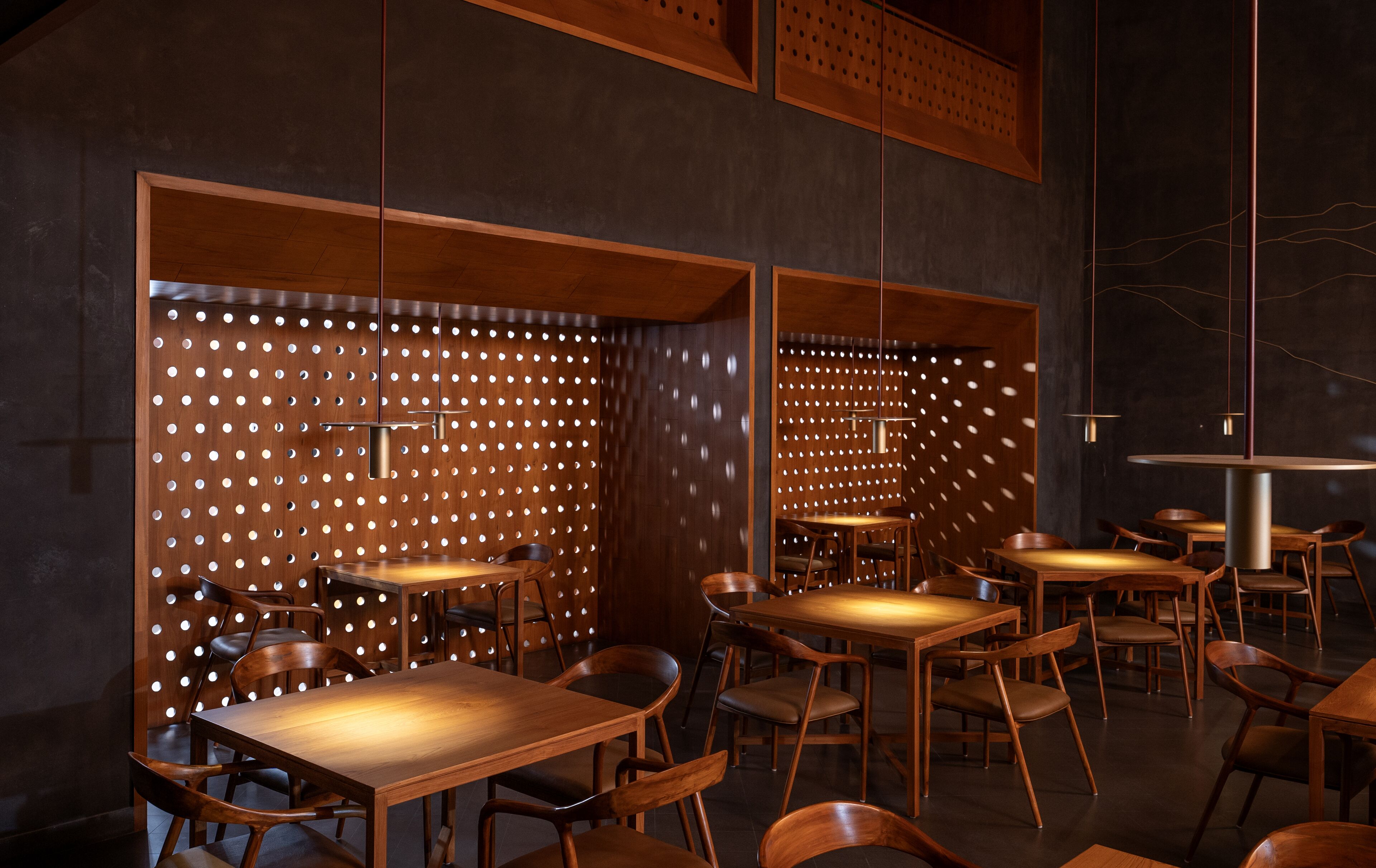A modern interior with wooden tables and chairs, a patterned wall, and hanging pendant lights.