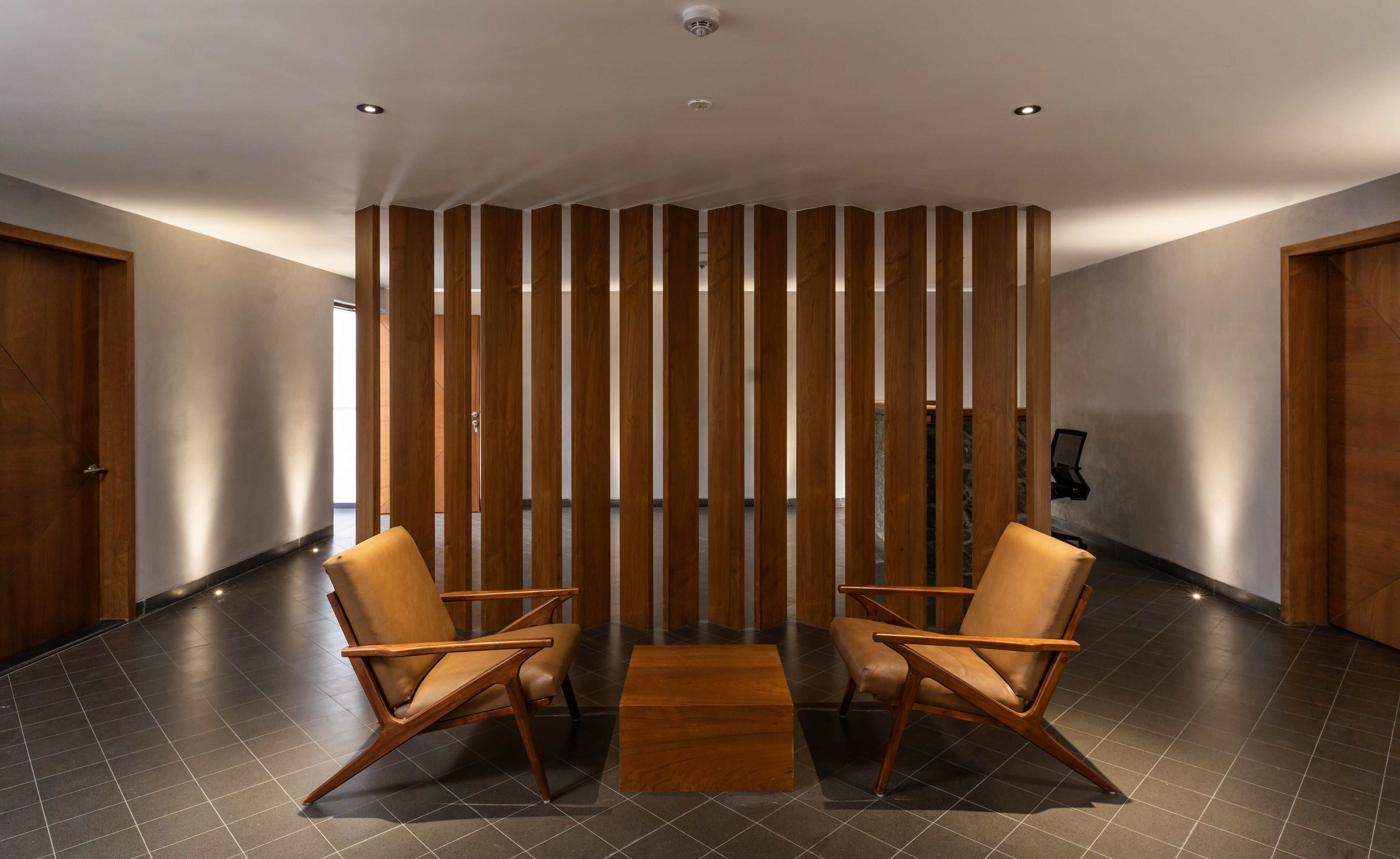 A modern interior with two leather chairs, a wooden partition, and a tiled floor.
