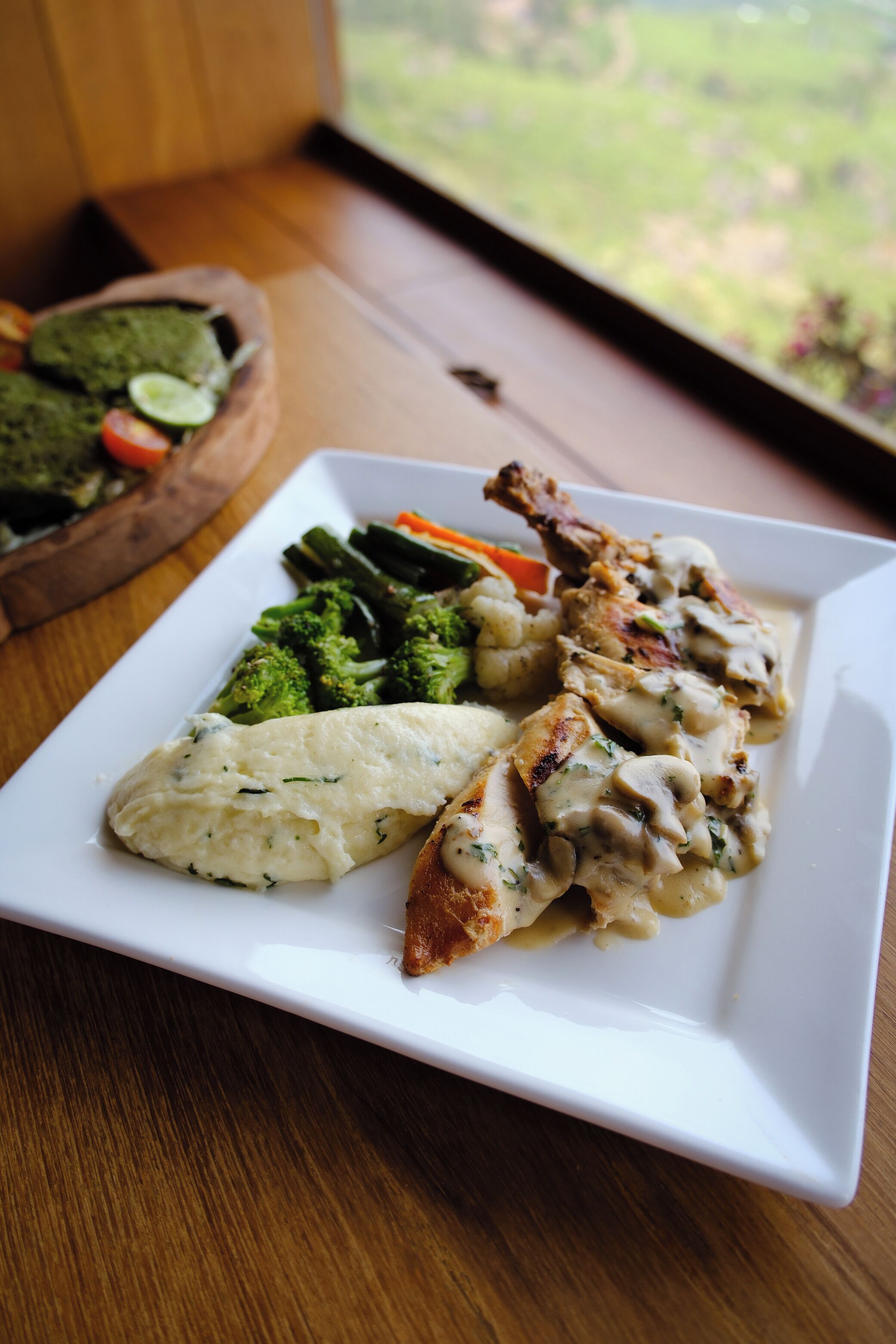 A plate of food with chicken, broccoli, carrots, and mashed potatoes on a white plate.