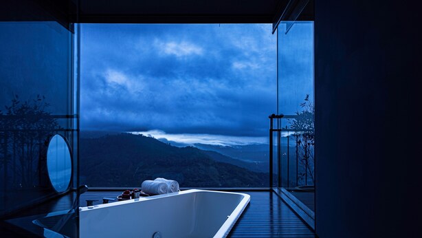 A modern bathroom with a large bathtub, a mirror, and a view of a mountainous landscape. - The Valle by Kondody Hotels (Devikolam)