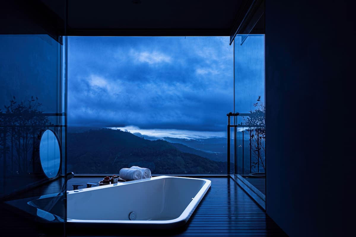 A modern bathroom with a large bathtub, a mirror, and a view of a mountainous landscape.