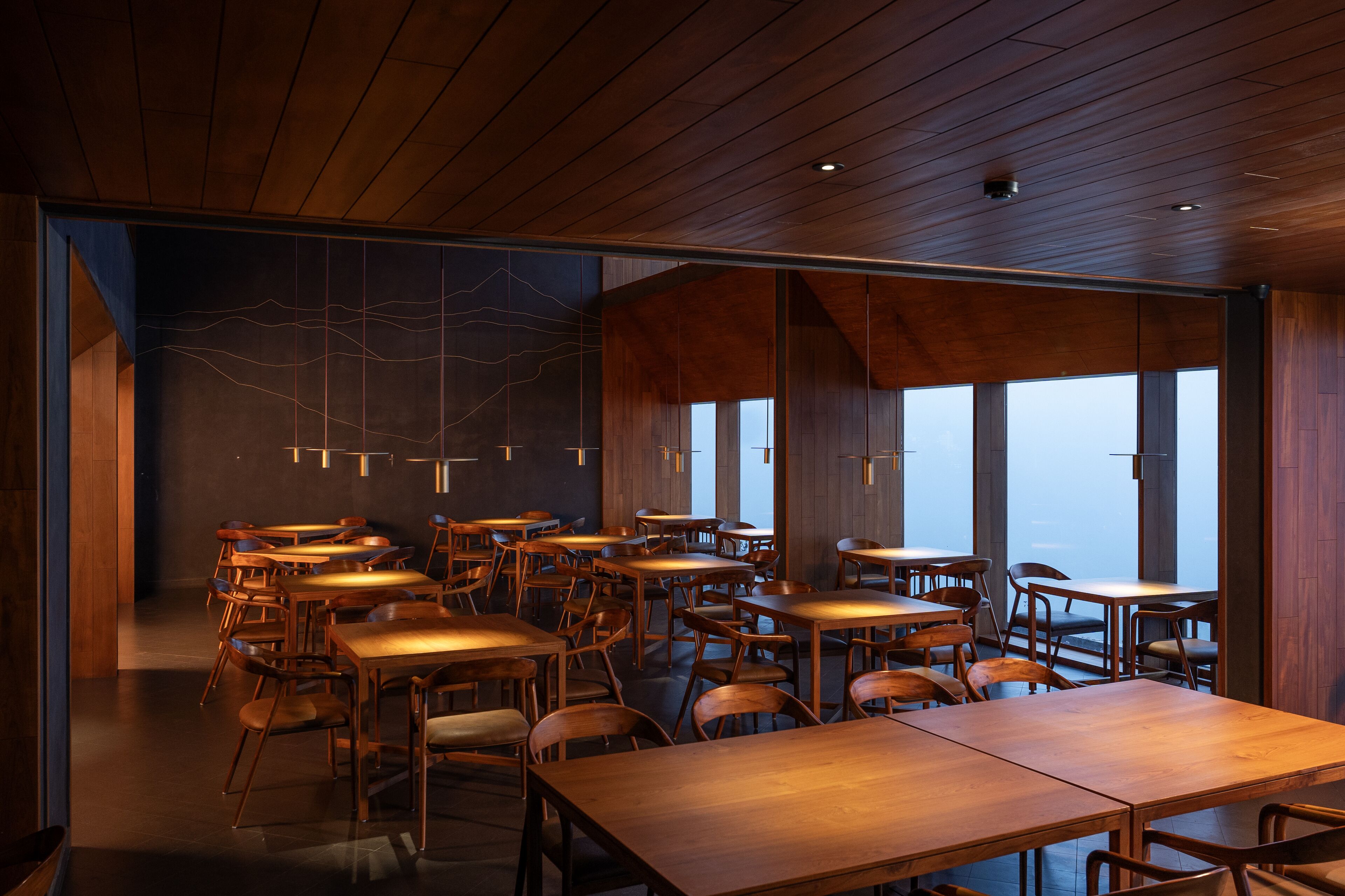 Un espace de restauration moderne avec des tables et des chaises en bois, de grandes fenêtres et un plafond haut.