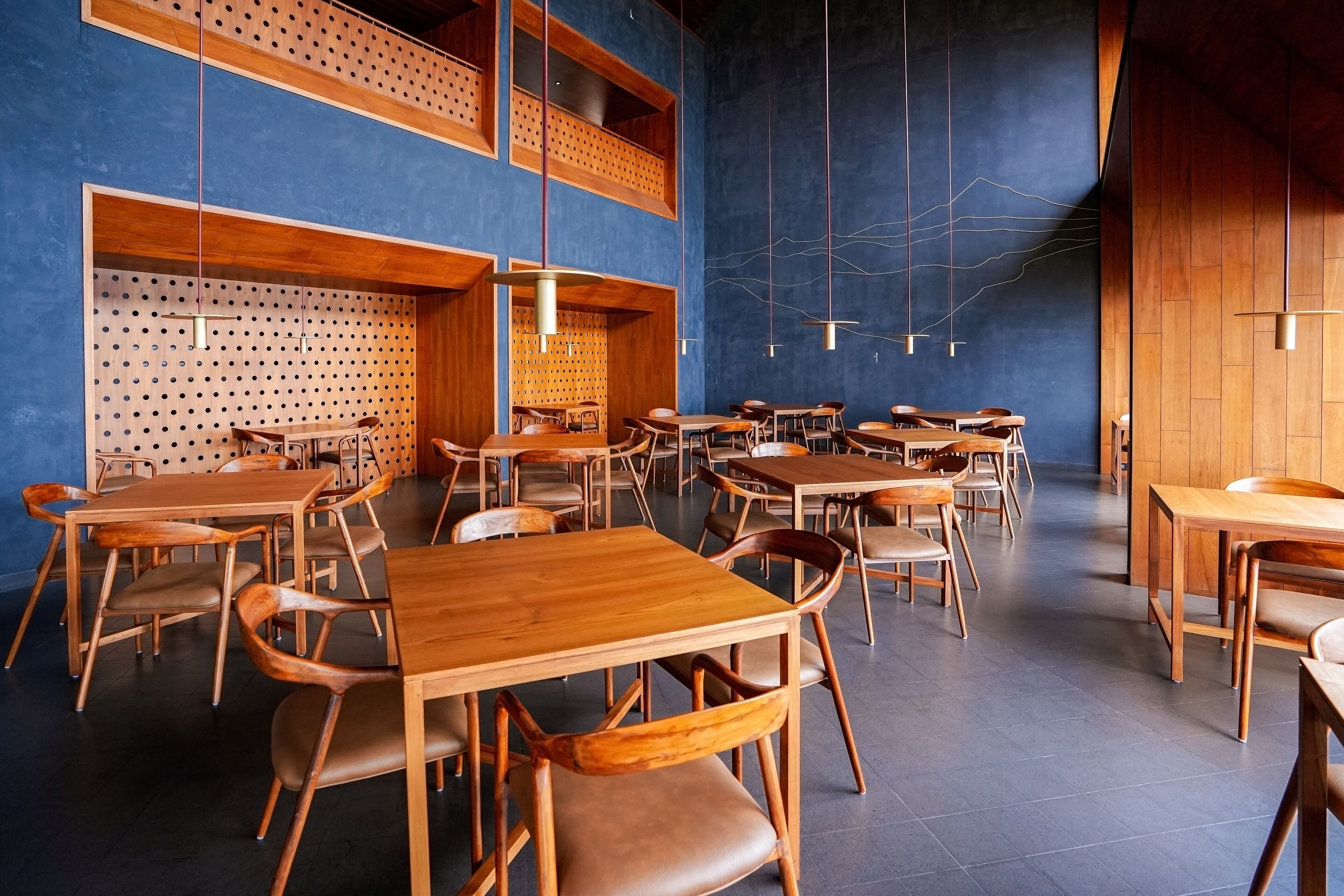 A spacious dining area with multiple wooden tables and chairs, high ceilings with exposed beams, and a blue accent wall.