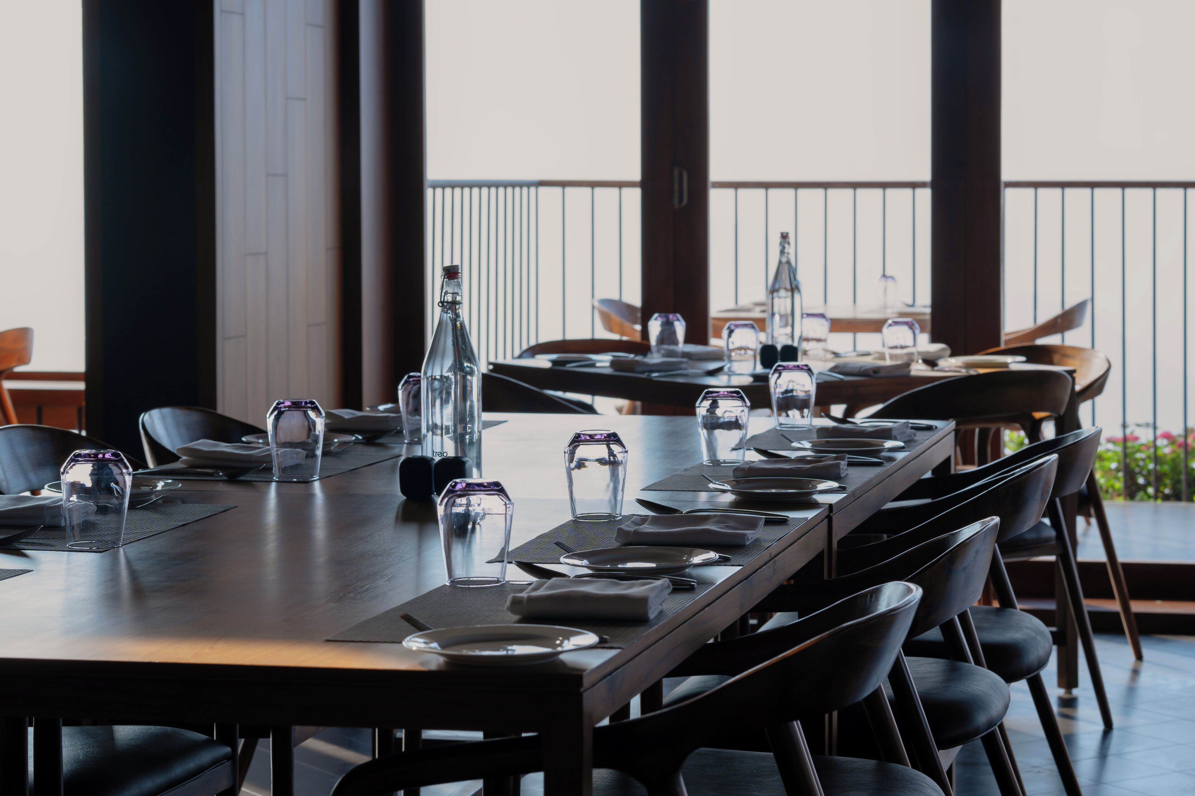 Un restaurante con mesas largas dispuestas para comer, vasos transparentes y botellas en cada mesa.