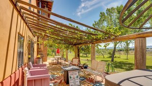 Ein Außenbereich mit Sitzgelegenheiten, einer Pergola, einem Hinweis auf eine Feuerstelle und Blick auf die umliegende Landschaft.