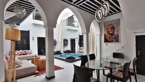 A spacious living area with a pool, modern furniture, and a glass dining table. - Riad Modern bed & breakfast  (Marrakech)