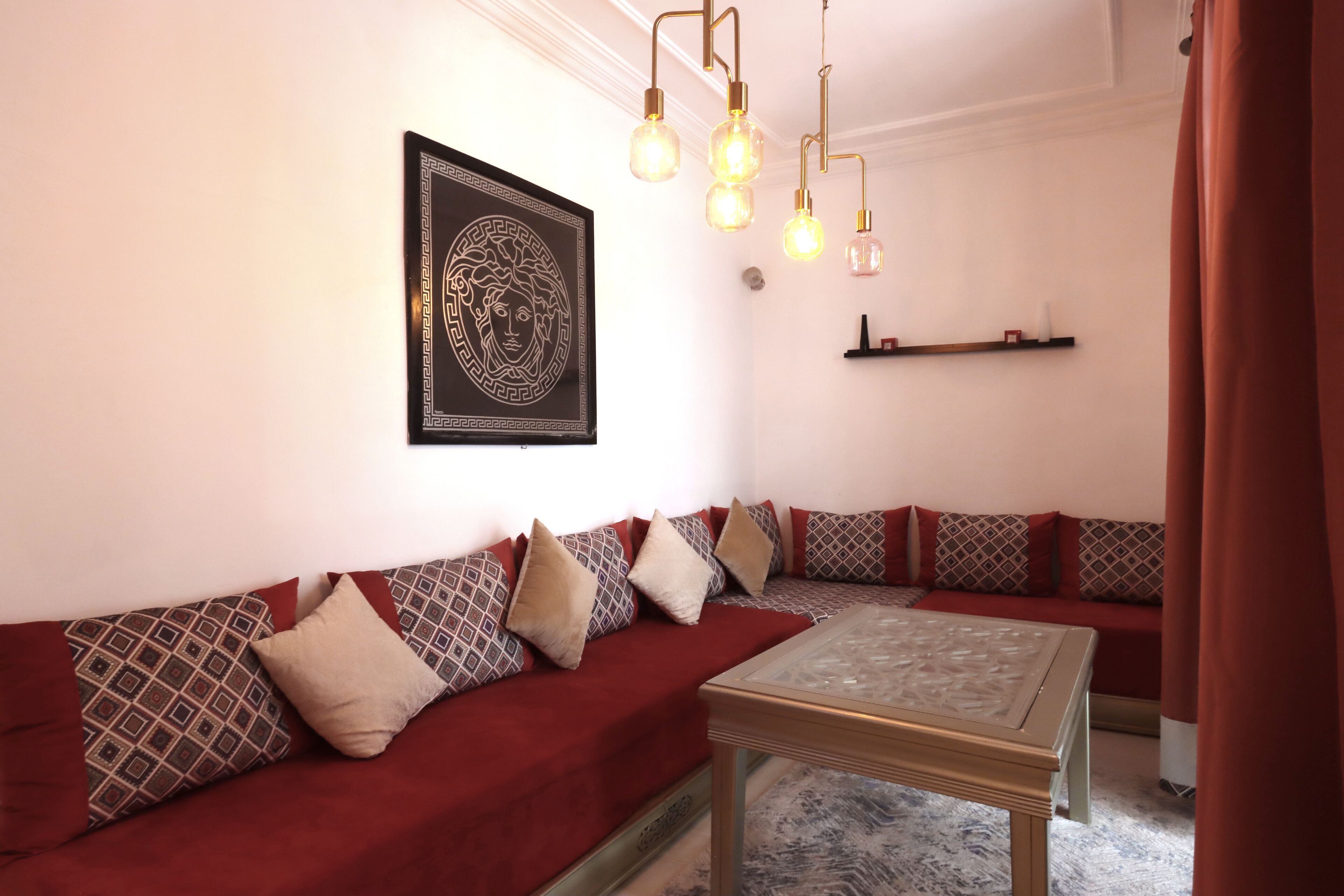 A modern living room with a red sofa, patterned cushions, a glass coffee table, and a decorative wall piece.