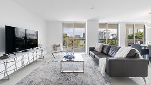 Ein modernes Wohnzimmer mit großem Flachbildfernseher, einer Couch, einem Couchtisch und einem Balkon mit Blick auf die Stadt.