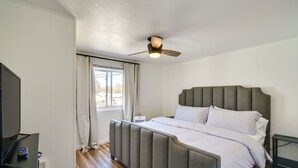 Quarto com cama, ventoinha no teto, janela com cortinas e televisão sobre um móvel.