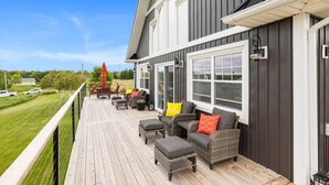 A covered outdoor deck with wicker furniture and a view of the surrounding area. - Heron House, Beautiful seaside retreat close to Cavendish (North Rustico)