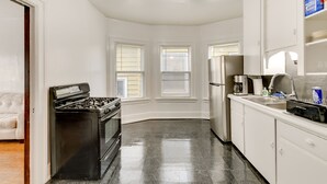 A kitchen with a stove, refrigerator, and sink. There are three windows with blinds, a ceiling fan, and a white countertop. - Charming Buffalo Apartment: 2 Mi to Downtown (Buffalo)