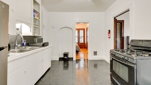 A kitchen with white cabinets, a stove, and a microwave. There is a trash can and a ceiling fan. - Charming Buffalo Apartment: 2 Mi to Downtown (Buffalo)