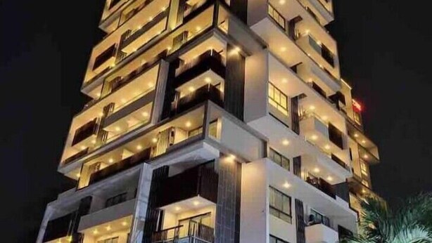 A multi-story building with a modern architectural design, featuring balconies and illuminated windows. - Beautiful & Spacious 1 BR Suite - Modern African Decor & Ocean View, Osu (Accra)