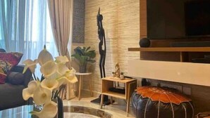 A modern living room with a sofa, a coffee table, and a TV mounted on a textured wall. - Beautiful & Spacious 1 BR Suite - Modern African Decor & Ocean View, Osu (Accra)
