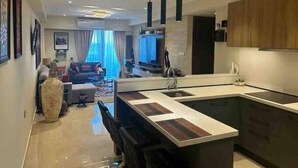 A modern kitchen with a central island, pendant lighting, and a dining area with a sofa and coffee table. - Beautiful & Spacious 1 BR Suite - Modern African Decor & Ocean View, Osu (Accra)
