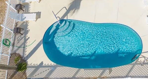 An aerial view of a swimming pool with a surrounding deck and lounge chairs.