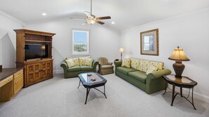 A living room with a television, two green sofas, a coffee table, a ceiling fan, and a lamp.