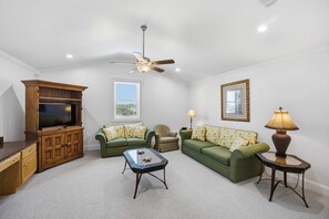 A living room with a television, two green sofas, a coffee table, a ceiling fan, and a lamp.